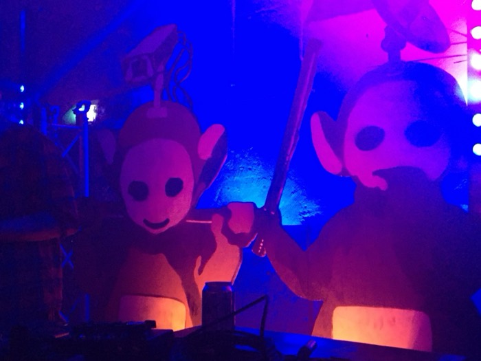 Giant Teletubbies-style figures with CCTV and machete under club lights