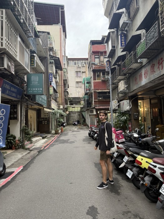 Joshua: standing in Taipei back alley, scooters, neon shop signs
