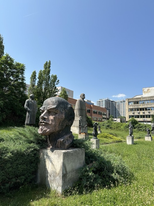 Socialist-era statue garden: giant Lenin head and figures on lawn, sunny day