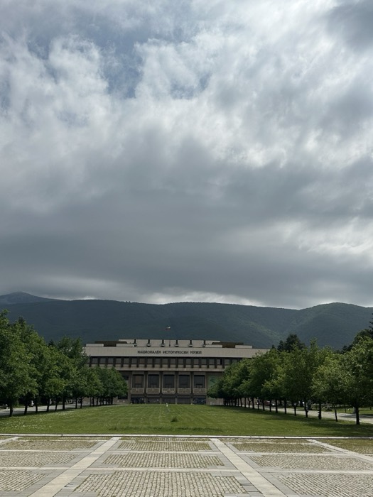 National History Museum: brutalist building below cloudy mountains, long stone plaza