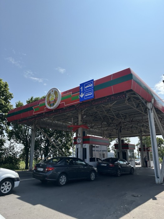 Transnistria PMR border crossing canopy, red-green flag colours, Soviet crest, cars