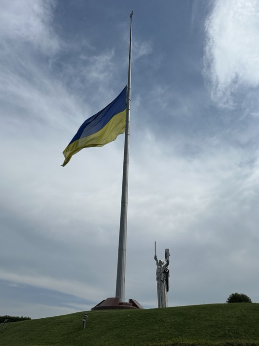 Giant Ukrainian flag on tall pole beside Motherland Monument on hill