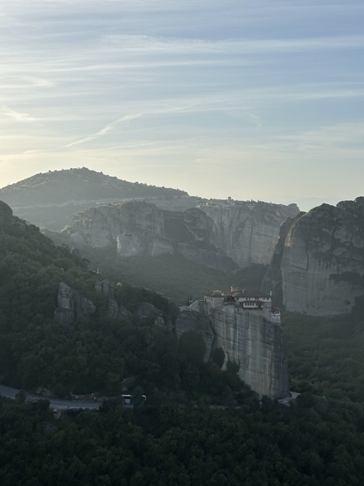 Misty dawn Meteora monastery clinging to sheer cliff face