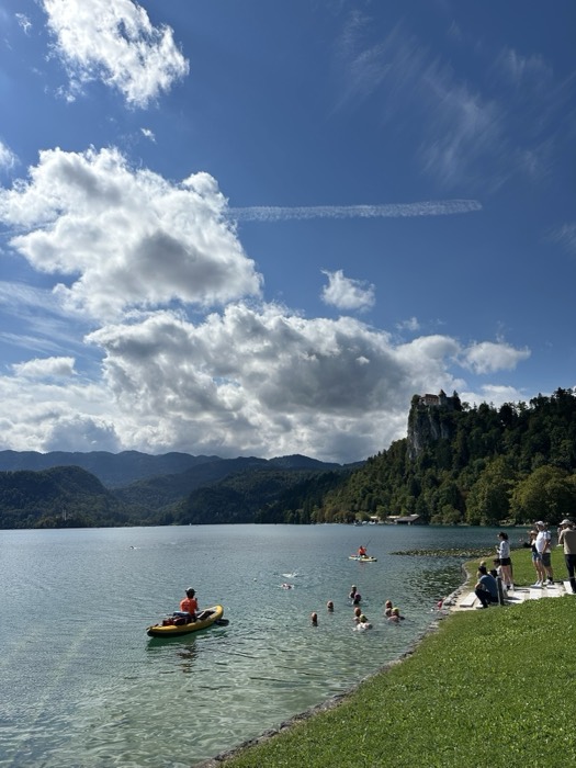 Lake Bled with clifftop Bled Castle, swimmers and kayaks, bright day