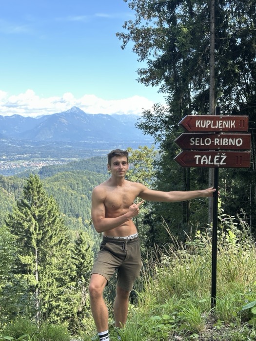 Shirtless friend from behind gazing at mountain panorama beside trail sign