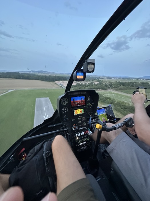Helicopter cockpit instrument panel low over fields, village ahead, dusk