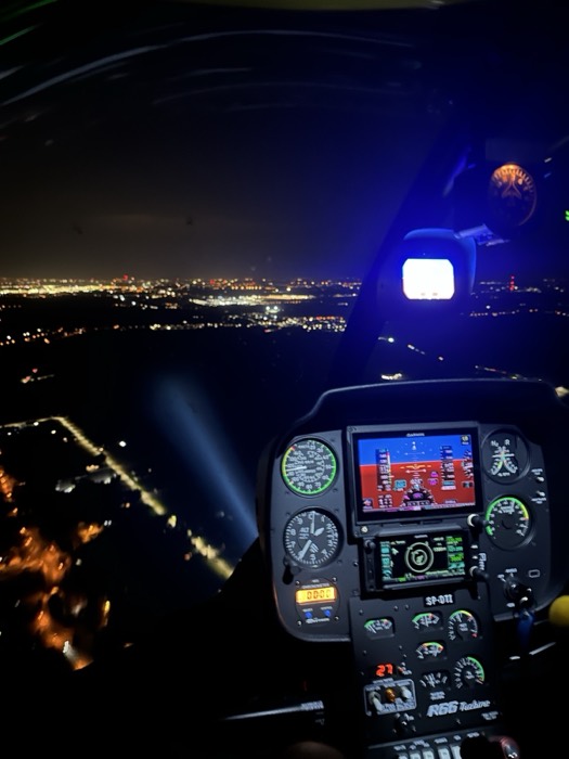 Night helicopter flight, city lights below and glowing cockpit instruments