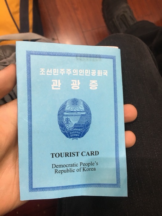 Hand holding DPRK Tourist Card, striking North Korea travel artifact