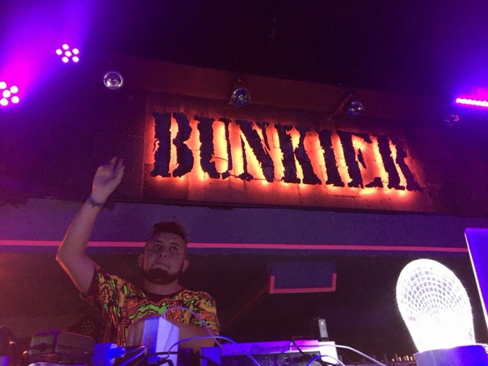 DJ raising hand under glowing BUNKIER club sign