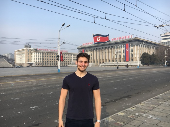 Joshua: smiling in t-shirt at Kim Il-sung Square, flag-draped ministry behind