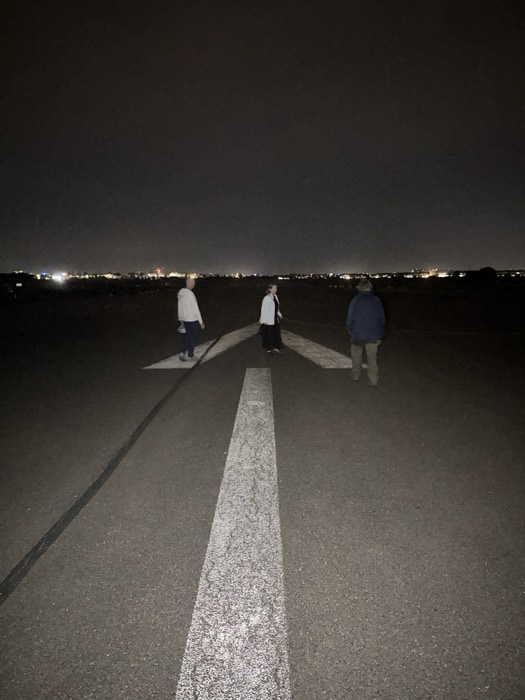 Three friends standing on dark Tempelhof runway arrow, city skyline