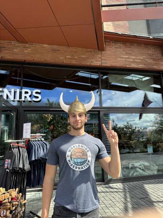 Joshua: wearing golden Viking horned helmet, peace sign, souvenir shop.