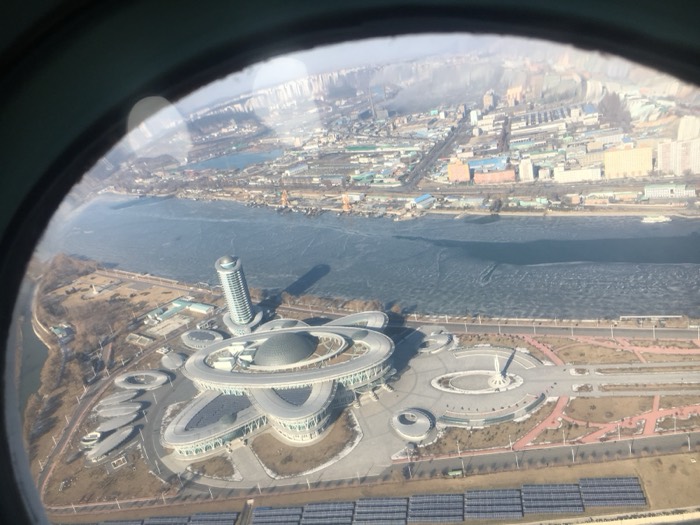Aerial of Pyongyang Sci-Tech Complex atom-shaped building through porthole window