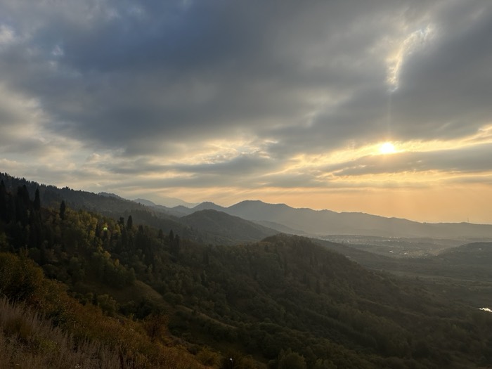 Golden-hour sun rays over forested mountain ridges and hazy valley