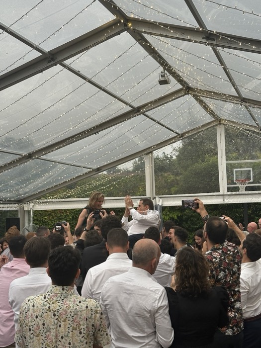 Couple lifted on shoulders amid crowd at marquee wedding party