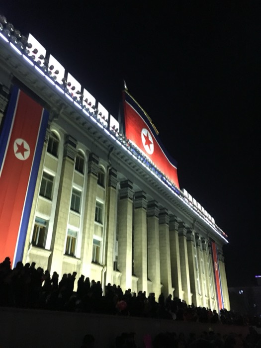 Floodlit columned NK building with giant flags at night