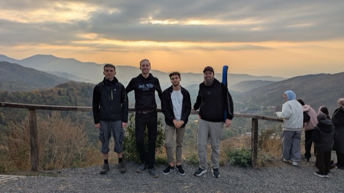 Joshua: with three friends at mountain viewpoint railing, sunset behind