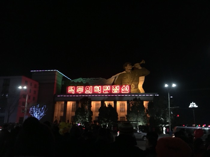 Neon-lit building with bugler statue and Korean slogan, NYE crowd