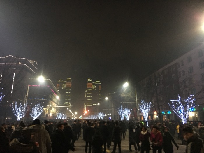 New Year crowd on lit boulevard with twin towers behind