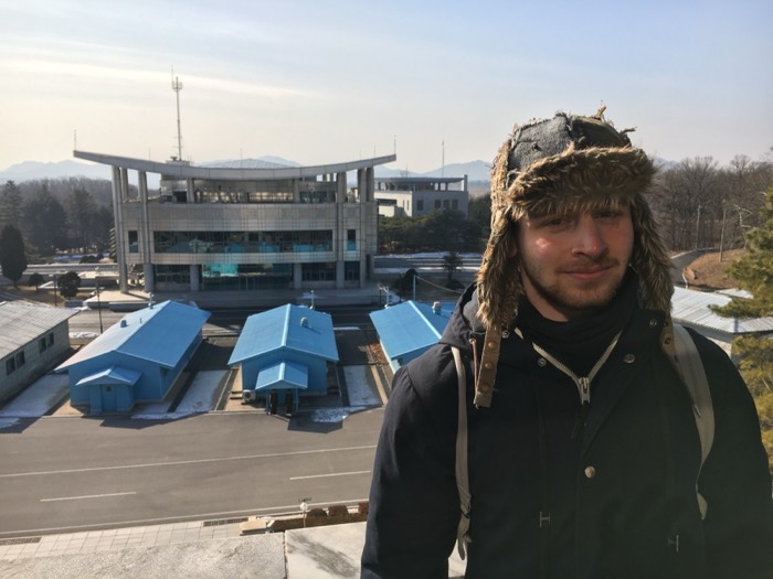 Joshua: fur hat portrait above blue JSA buildings at DMZ
