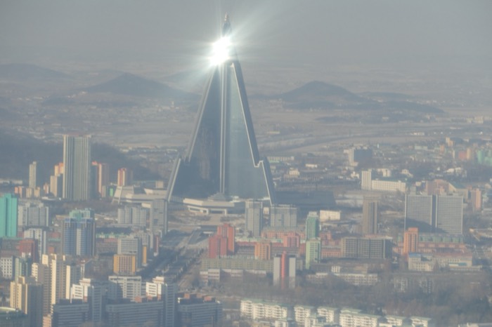 Iconic Ryugyong Hotel pyramid skyscraper rising over hazy Pyongyang, sun glint on spire