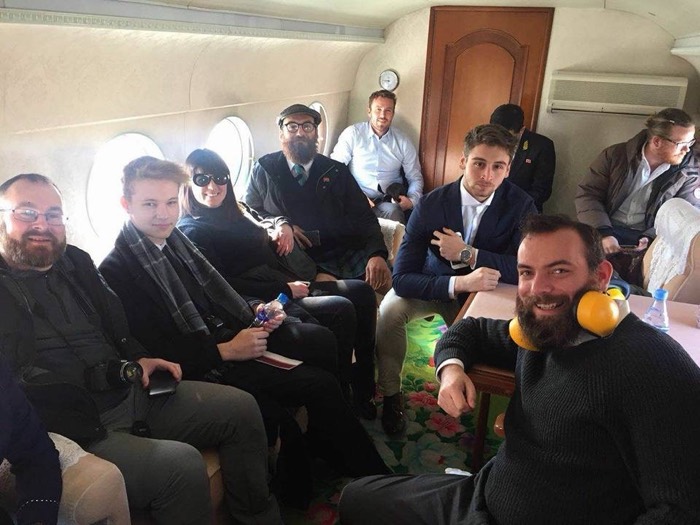 Joshua: in blue blazer with tour group seated inside floral-trimmed helicopter cabin