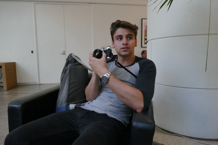Joshua: candid in armchair holding a vintage film SLR camera.