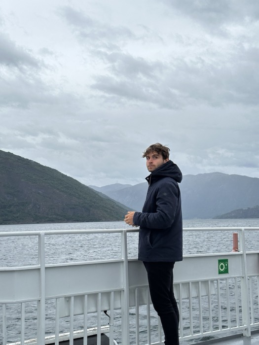 Joshua: on a ferry deck before grey Norwegian fjord and mountains