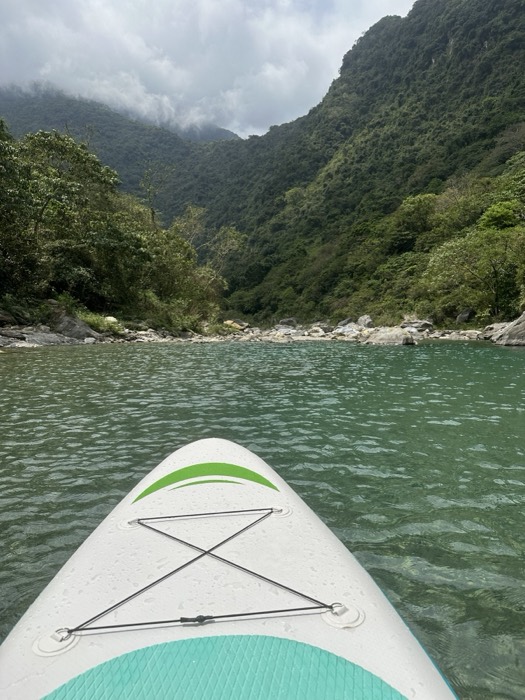 Paddleboard POV gliding up jungle river gorge, misty mountains