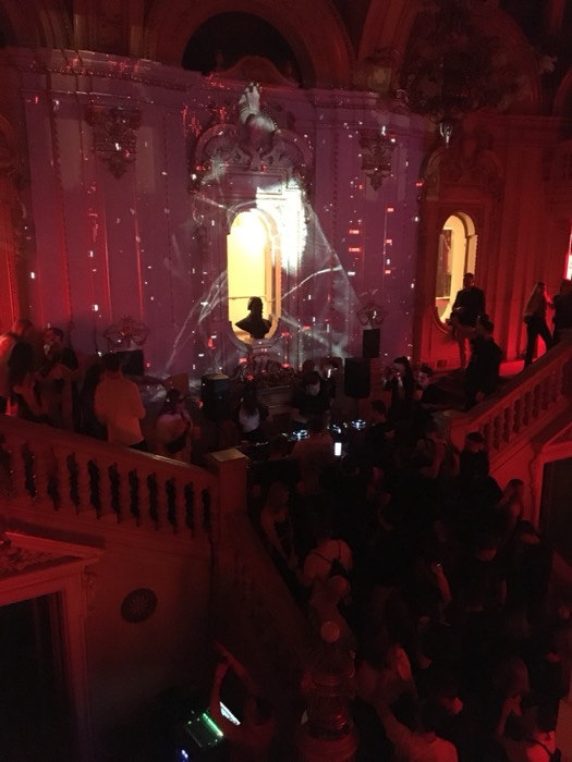 Crowd dancing under ornate palace hall with red light projection