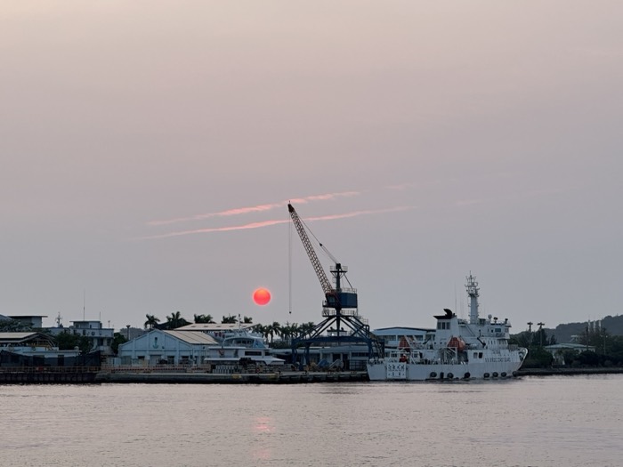 Red sun setting over harbor with crane and coast guard ship