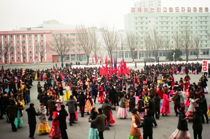 Mass dance in colorful hanbok with red flags, Pyongyang square