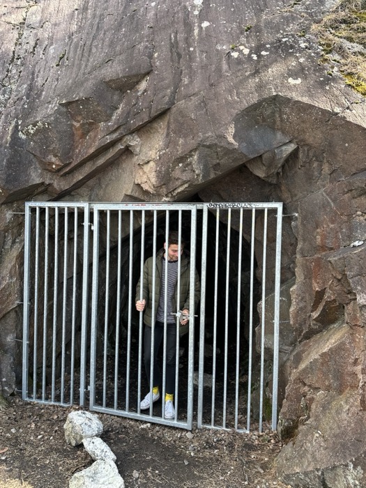 Joshua: standing inside barred cave entrance gate set in rock face