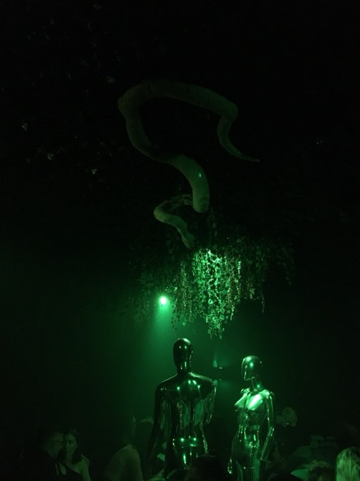 Green-lit chrome mannequins and surreal sculpture in bar