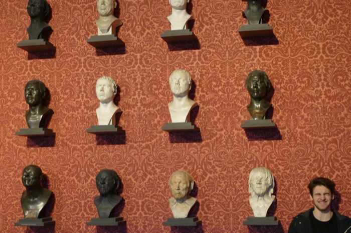 Joshua: peeking at grid of Roman emperor busts on red wall