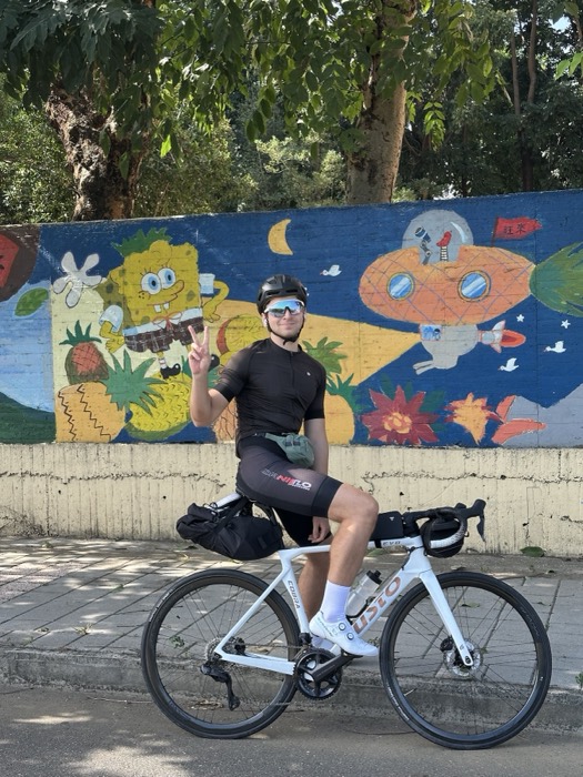 Joshua: in cycling kit flashing peace sign on road bike by SpongeBob mural
