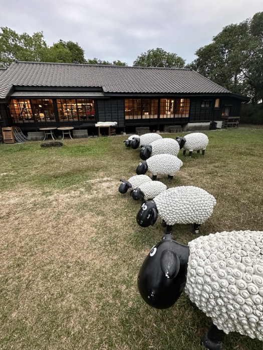 Quirky Shaun-the-Sheep sculptures grazing outside a black wooden cafe