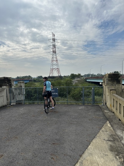 Joshua: pausing on bike near pylon and river bridge