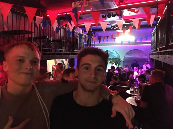 Joshua: with friend in a bunting-strung club, crowd and stage lights behind