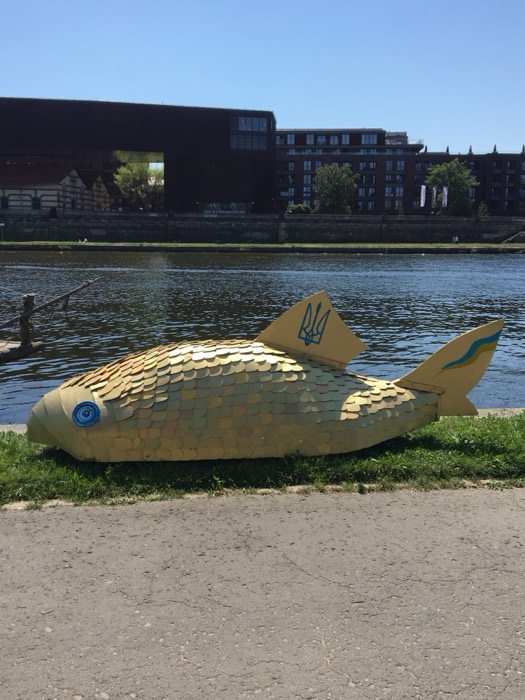 Golden scaled fish sculpture with Ukrainian trident by riverbank