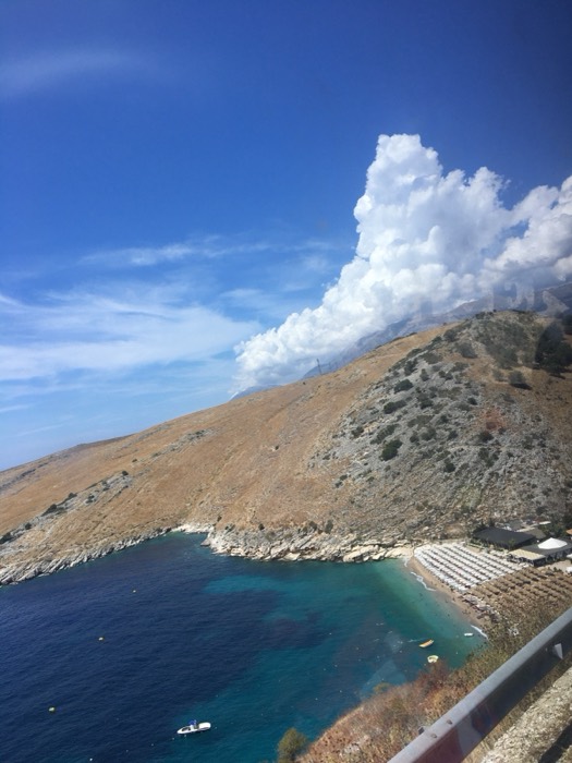Turquoise cove with beach umbrellas below arid coastal cliffs, Albanian Riviera