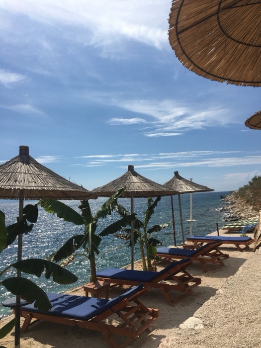Thatched parasols and blue loungers over sparkling sea, Albanian beach club