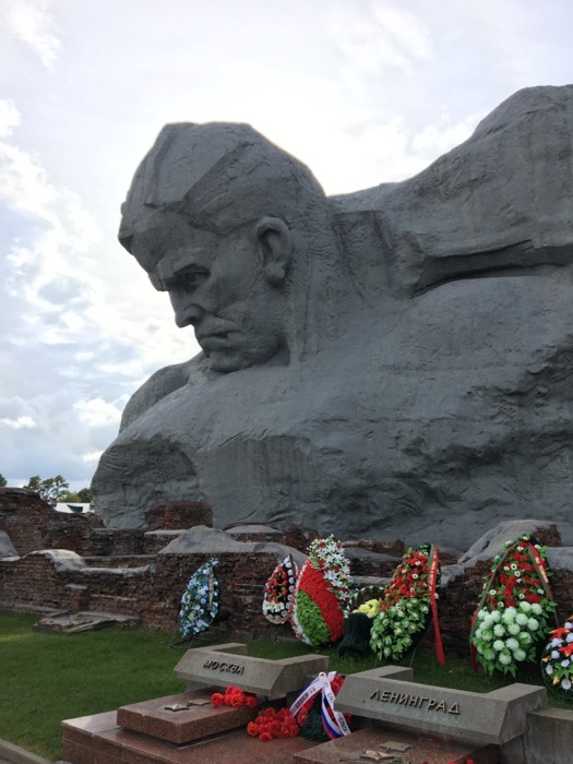 Colossal Courage soldier head sculpture over fortress ruins, wreaths