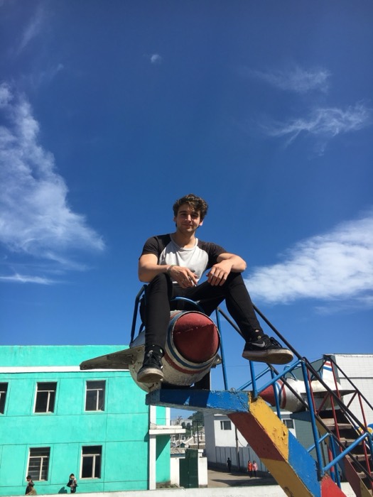 Joshua: perched atop rocket-shaped playground slide, blue sky, North Korea