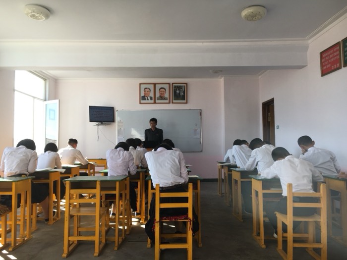 North Korean classroom, students at desks under Kim leader portraits