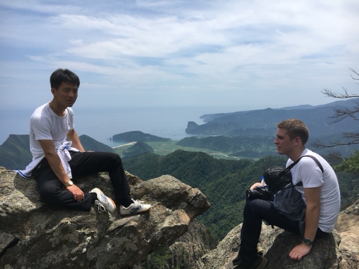 Joshua: with Korean guide on clifftop, coastline and sea behind