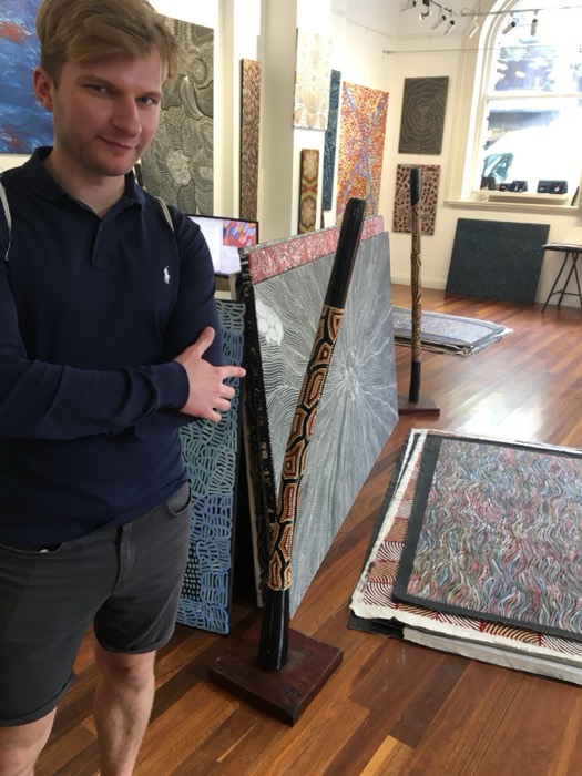 Joshua: holding canvas amid Aboriginal dot-paintings in gallery.