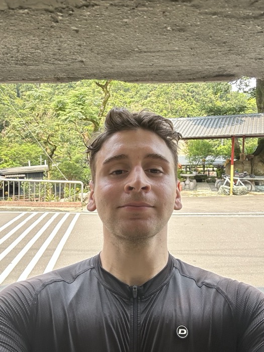 Joshua: sweaty cycling selfie in grey jersey, Taiwan mountain rest stop behind