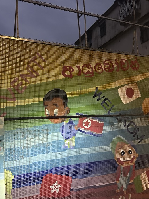 Colourful pixel-tile street mural lit at dusk below a building