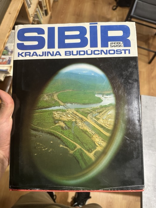 Holding vintage Slovak book 'Sibir - Krajina Buducnosti' with aerial cover.
